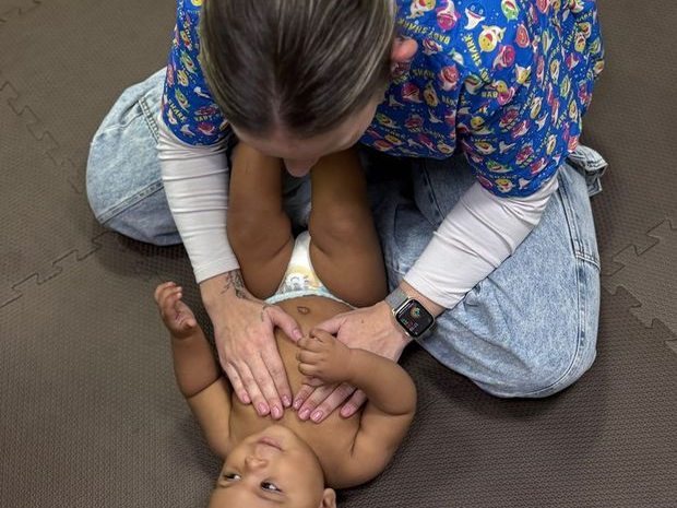 Mobilização suave na região abdominal de um bebê deitado de barriga para cima