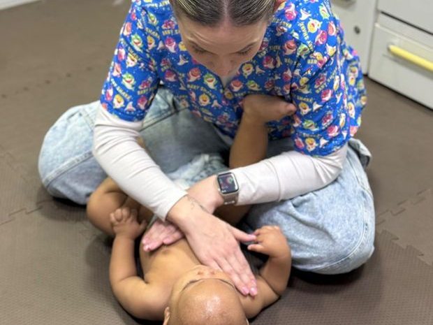 Fisioterapeuta aplicando terapia manual suave no tronco de um bebê deitado no tatame