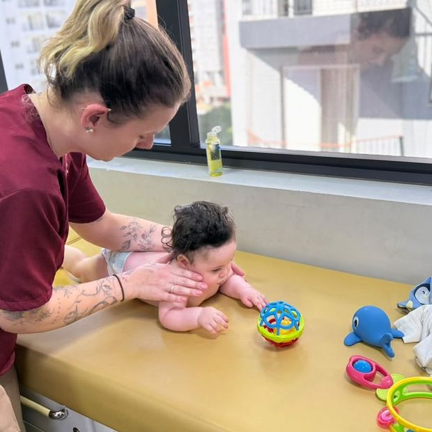 Bebê em decúbito ventral apoiado nos antebraços alcançando brinquedos